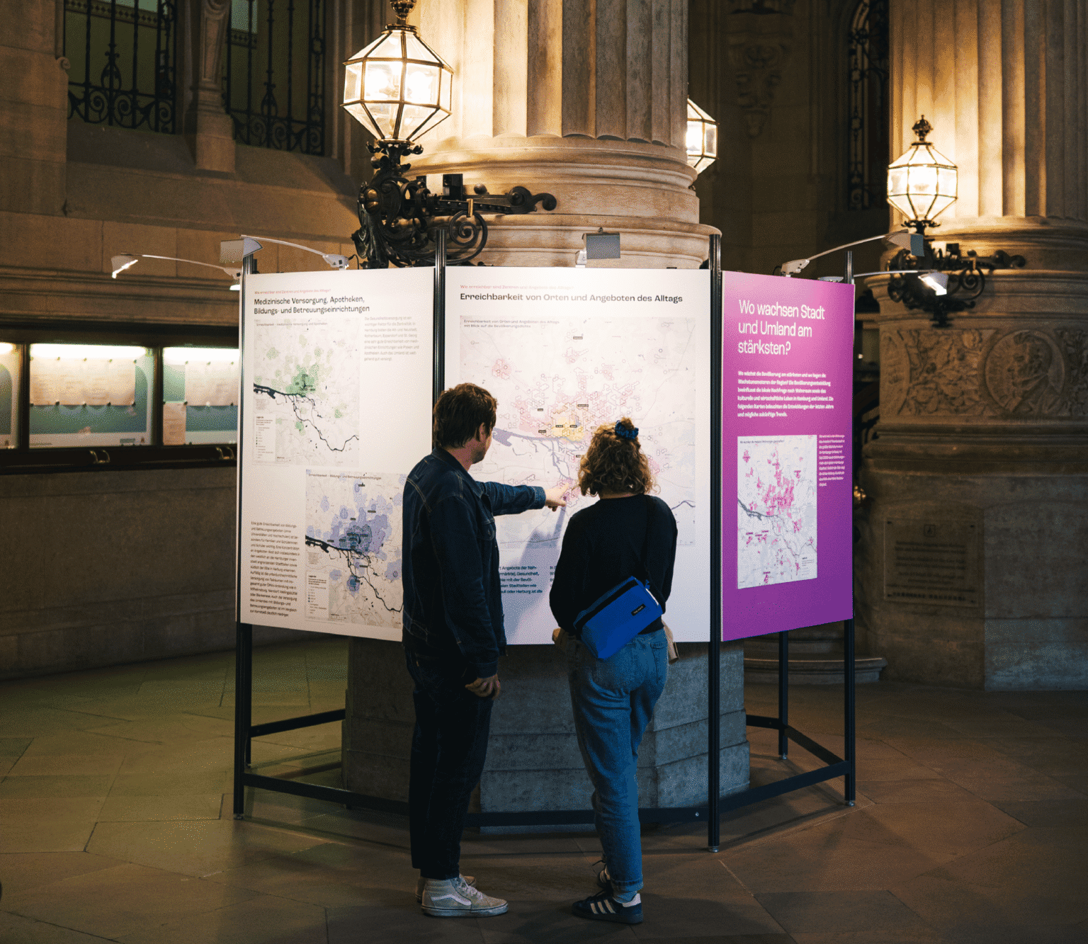 Zwei Personen betrachten in einem historischen Gebäude Ausstellungstafeln mit Karten und Texten zur Stadt- und Umlandentwicklung